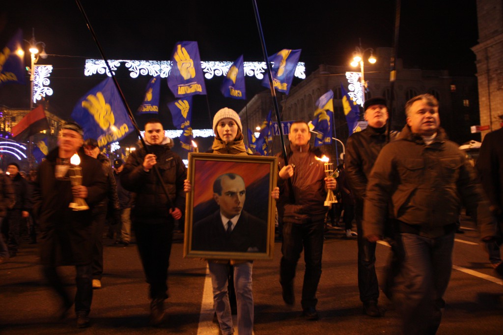 People holding UPA (horizontal red and black) and Svoboda (3 yellow fingers on blue) flags march through Kyiv to the honor of the Nazi ally, Bandera.